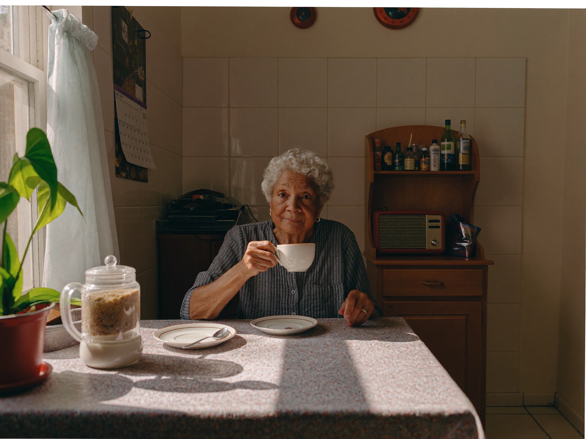 Older resident at her kitchen table with a cup of tea, soft window light